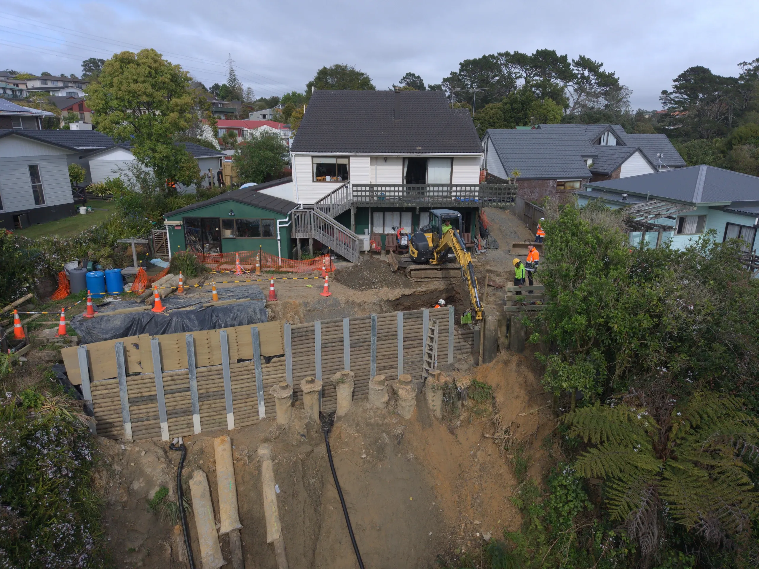 Aerial view of the Lynfield site, with the soldier pile and timber lagging wall running the length of the slope below the house and the excavated slip face beyond.