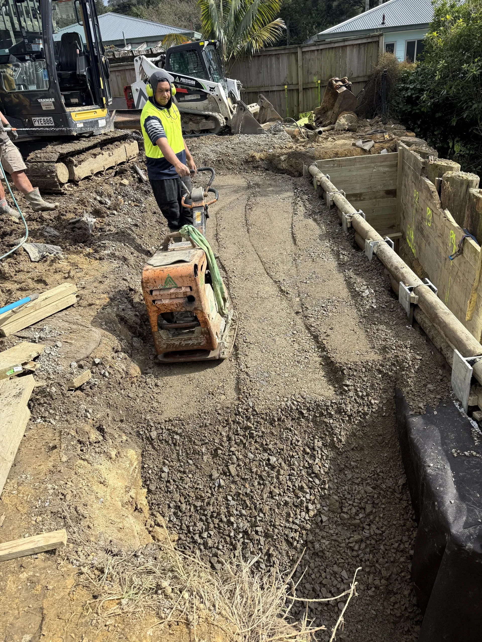 Compacting the base course alongside the completed timber retaining wall as the site is finished.