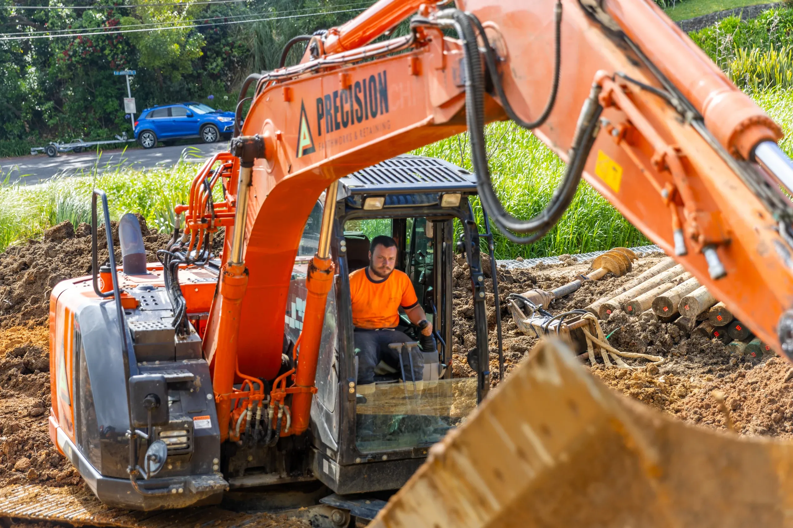 An excavator trimming the cut face beside the road, spoil stockpiled alongside the working platform.