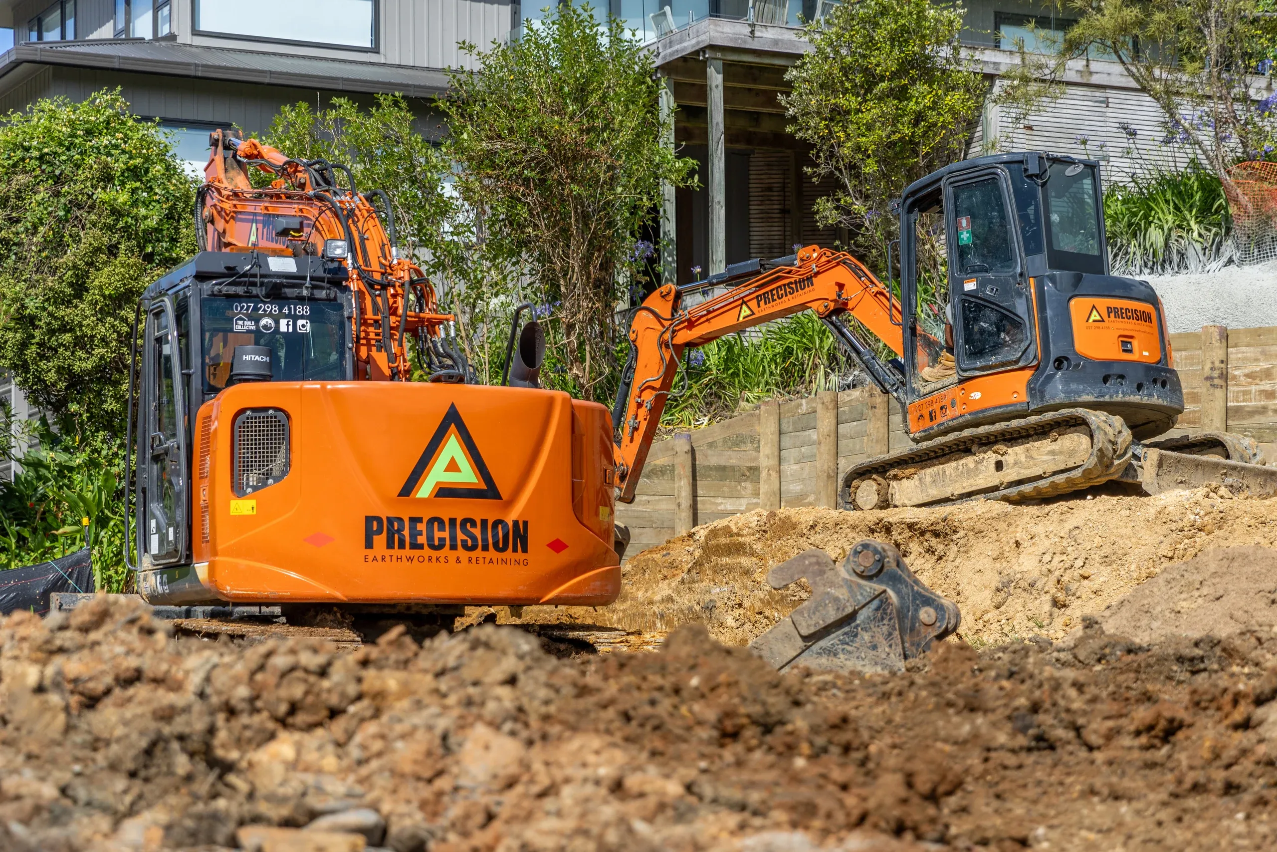 Two excavators working together to cut the first terrace into the coastal slope beside the house.