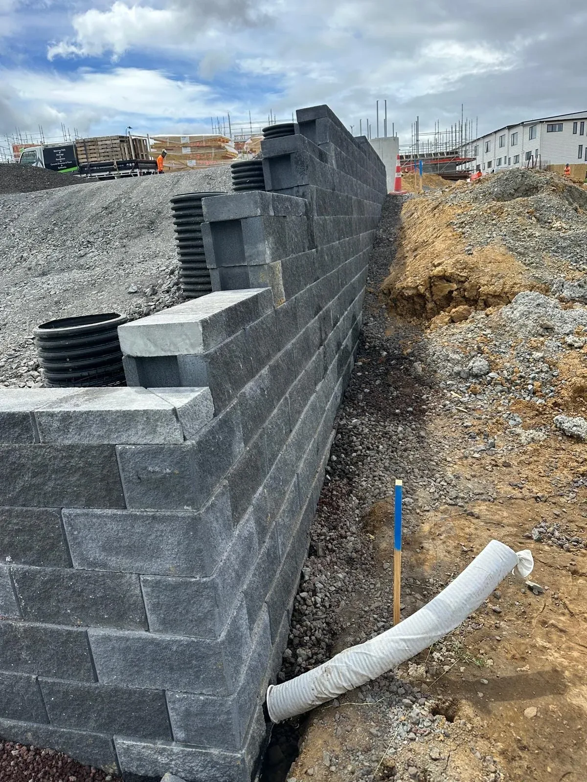 Keystone block wall stepping down the site, drainage risers and scoria backfill visible behind the blocks.
