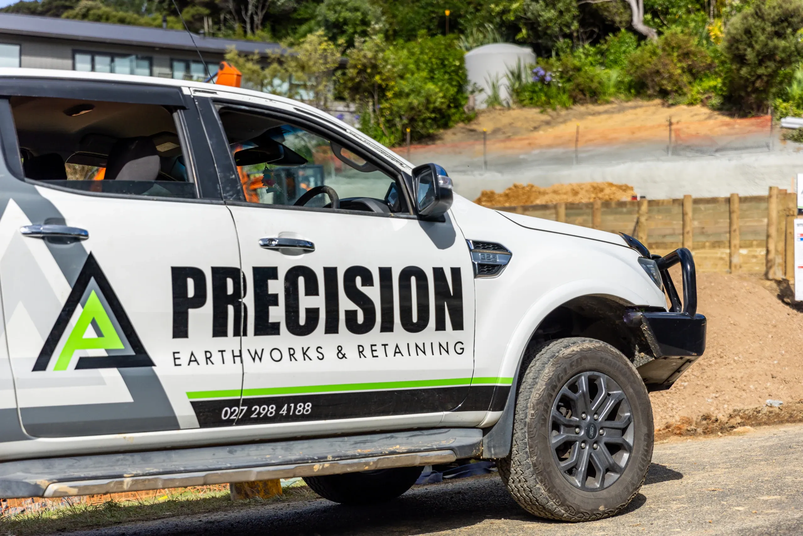 The branded Precision ute at the site entrance, timber retaining and cut ground visible up the slope.