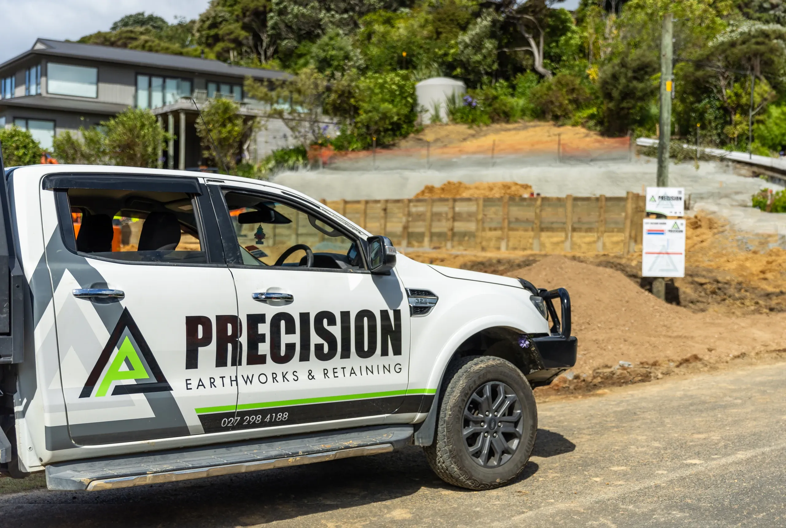 A Precision Earthworks ute parked at the Waiheke street frontage, with the freshly cut earth bank behind it.