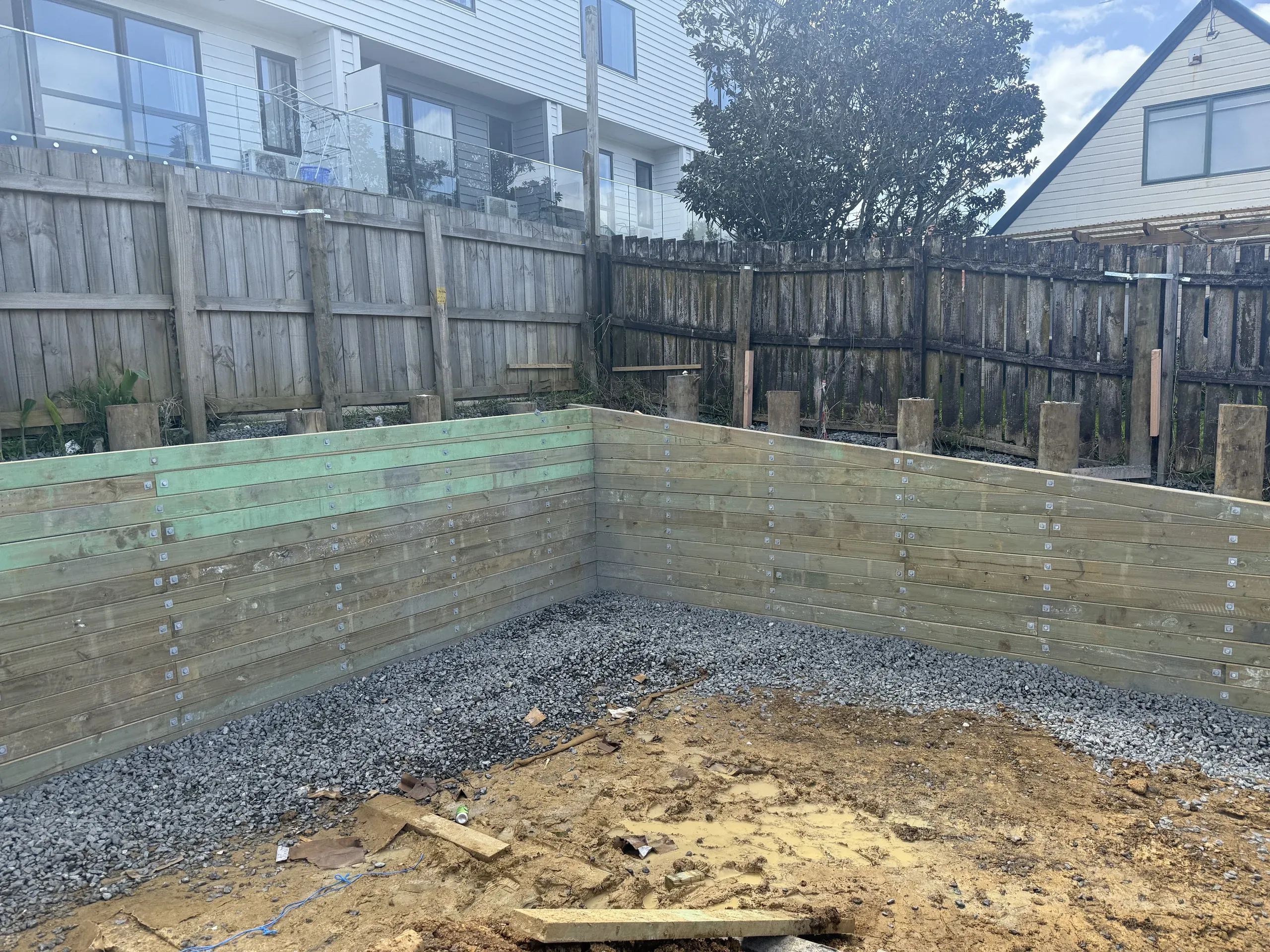 Timber retaining wall turning the corner of a building platform, drainage metal run along both faces.