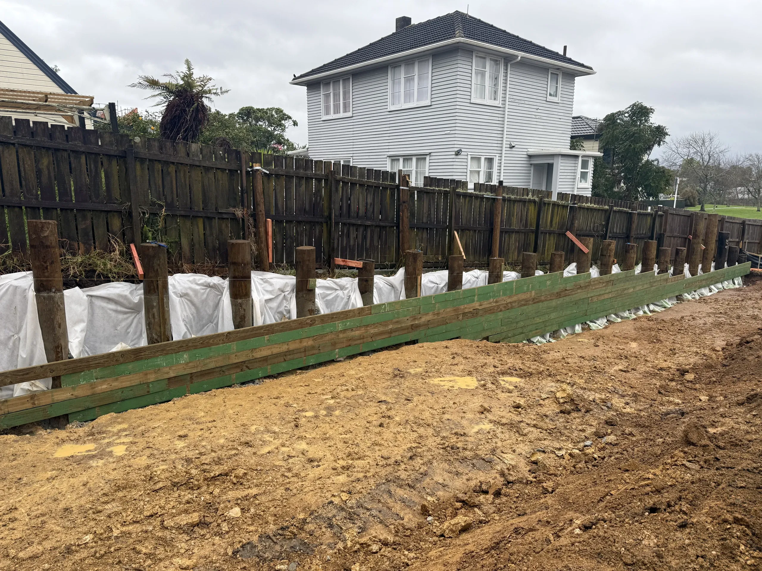 Timber retaining wall running the length of the boundary, posts set and drainage filter fabric in place behind.